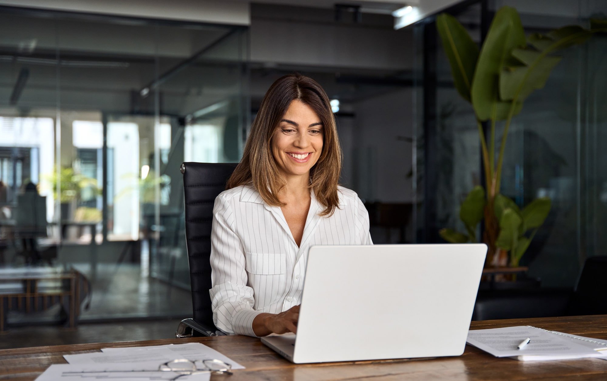 Geschäftsfrau in einem modernen Büro, die lächelnd an ihrem Laptop arbeitet.
