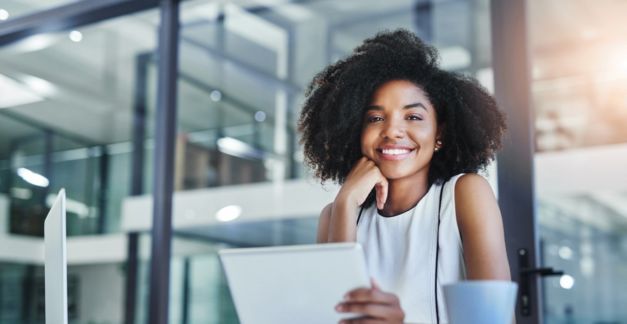 Junge Frau im modernen Büro, die freundlich in die Kamera lächelt und ein Tablet hält.