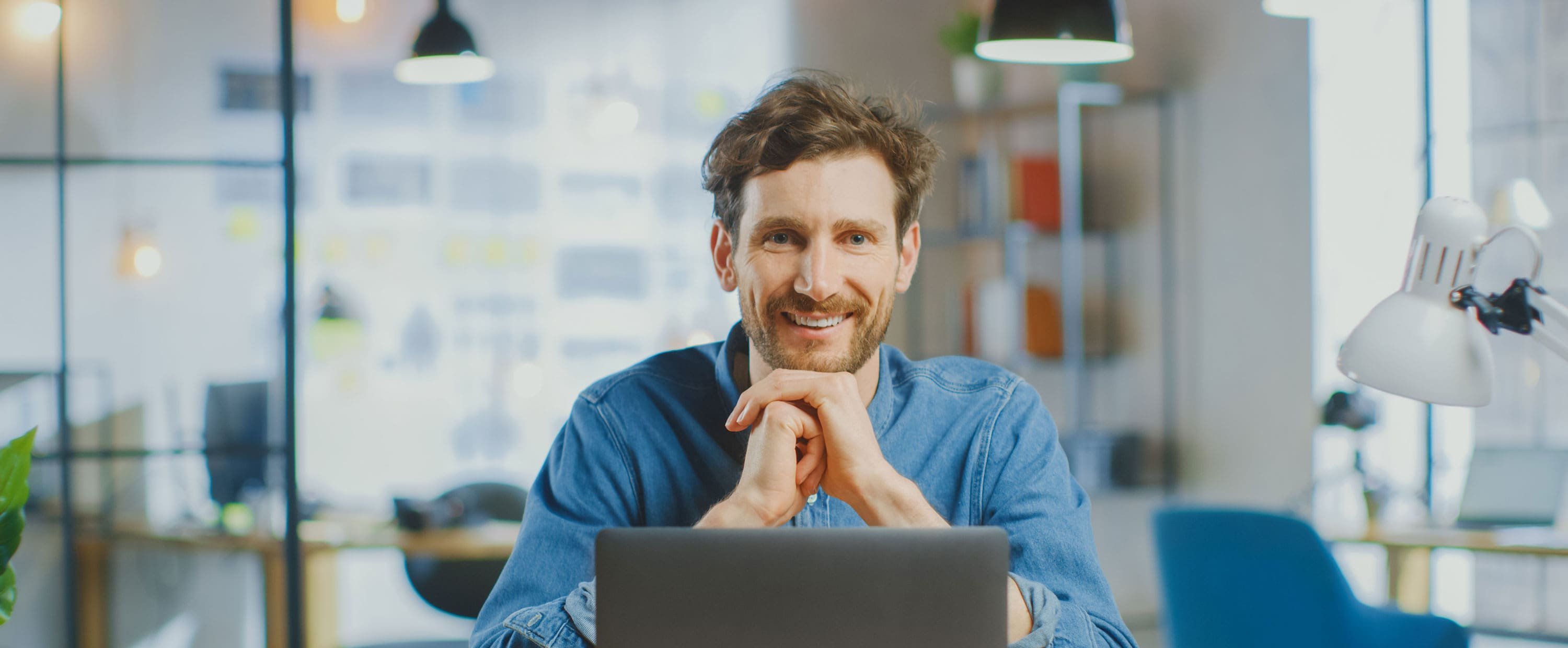 Junger Controlling-Mitarbeiter sitzt zufrieden vor seinem Laptop