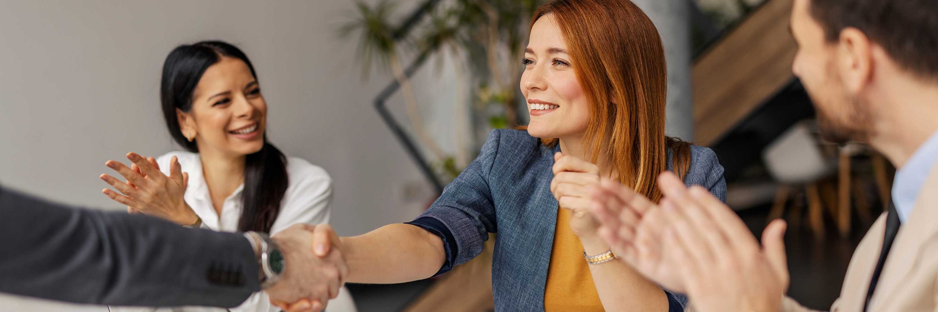 Žena s oranžovými vlasy se usmívá a podává ruku muži. Další muž tleská.