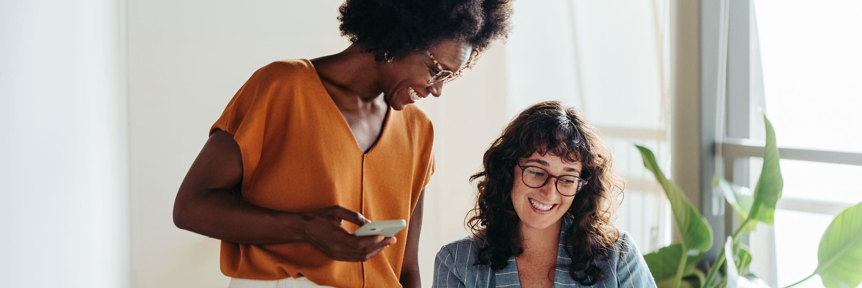 Két alkalmazott egy világos irodában, akik mosolyogva néznek együtt egy notebook képernyőjére.