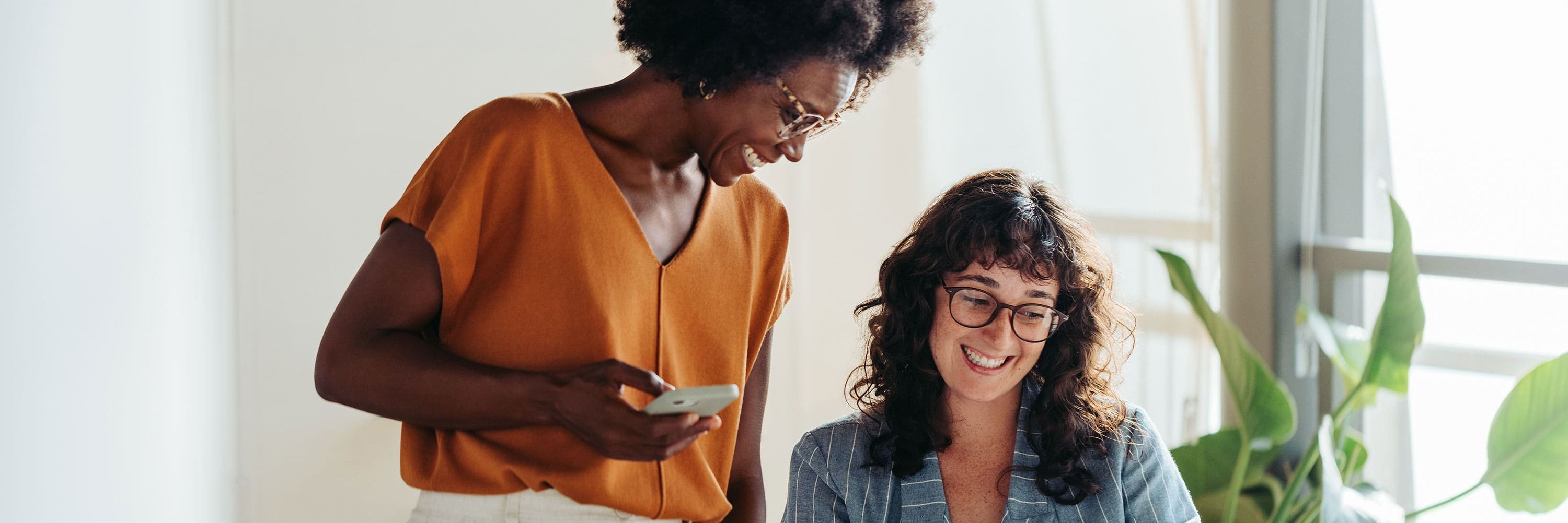 Két alkalmazott egy világos irodában, akik mosolyogva néznek együtt egy notebook képernyőjére.