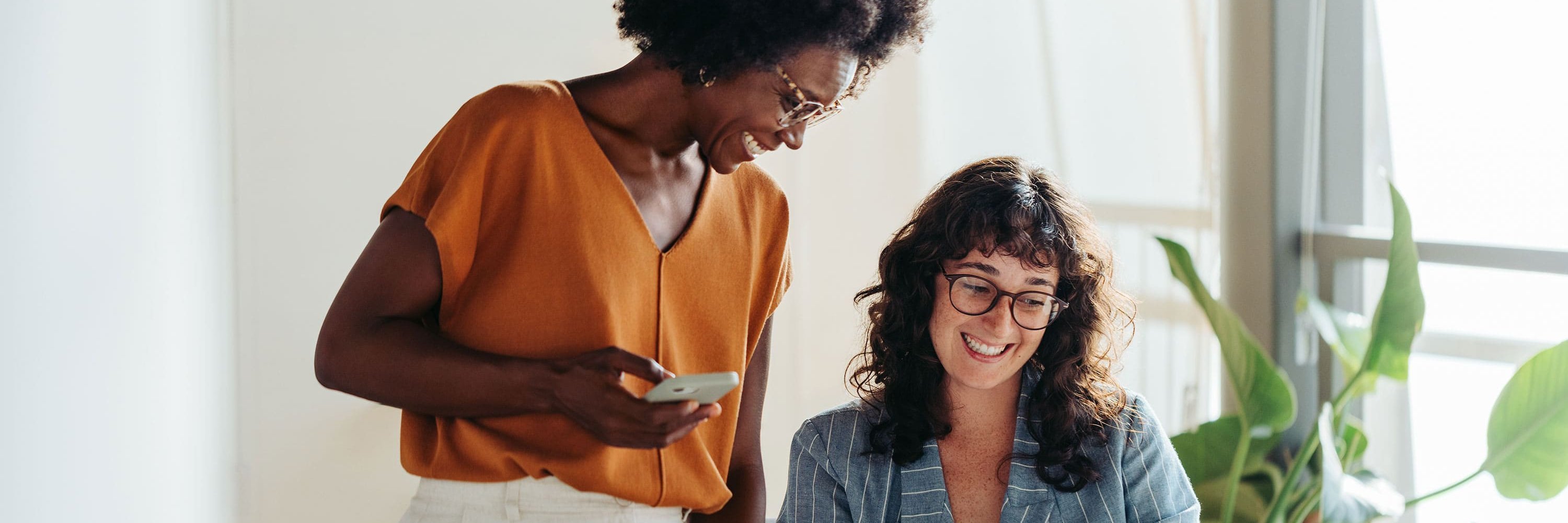 Két alkalmazott egy világos irodában, akik mosolyogva néznek együtt egy notebook képernyőjére.