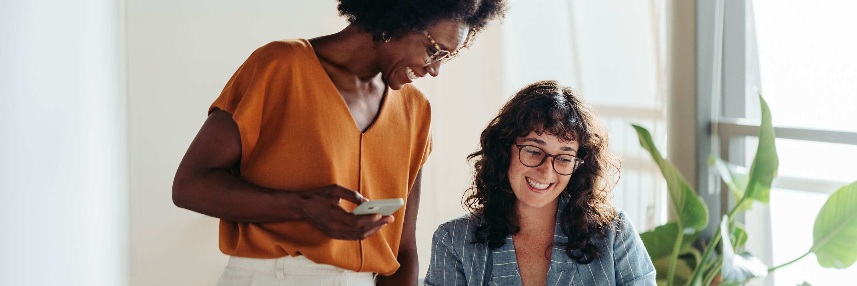 Két alkalmazott egy világos irodában, akik mosolyogva néznek együtt egy notebook képernyőjére.