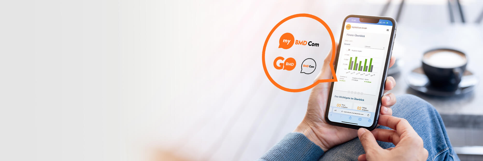 Person hält Smartphone mit BMD Com Finanzübersicht, daneben Logos von my BMD Com, App BMD Go und BMD Com. Im Hintergrund steht eine Kaffeetasse.