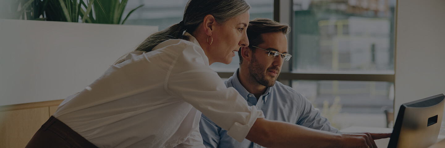 Frau und Mann im Büro, die auf einen Desktop blicken. 