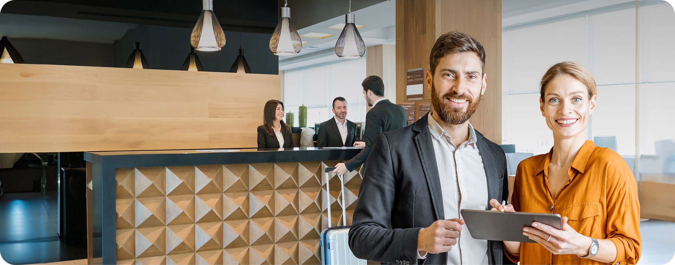 Eine Frau und ein Mann stehen mit einem Tablet in der Lobby eines Hotels. 