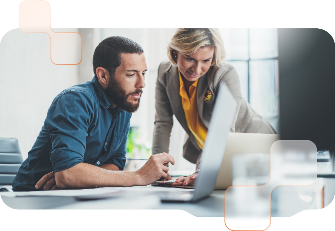 Sitzender Mitarbeiter und stehende Mitarbeiterin überlegen im Büro gemeinsam vor einem PC-Bildschirm.