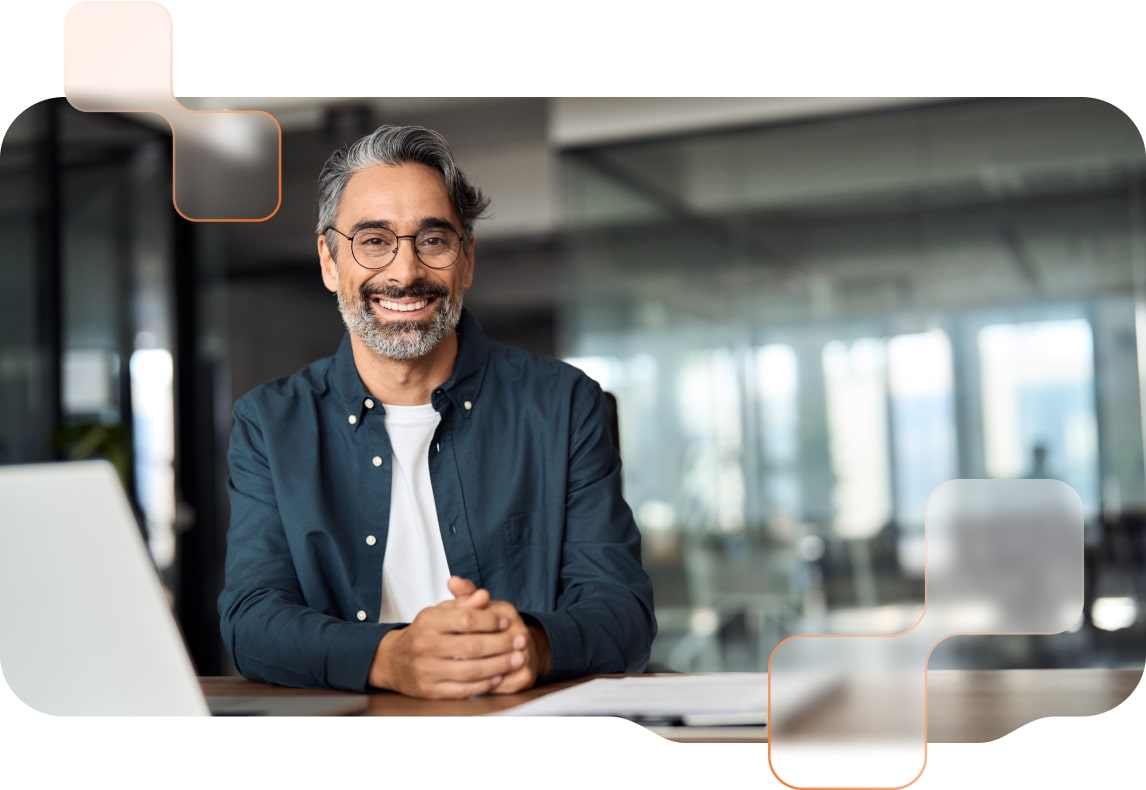 Mitarbeiter in einem modernen Büro, der lächelnd an seinem Schreibtisch vor seinem Laptop sitzt.