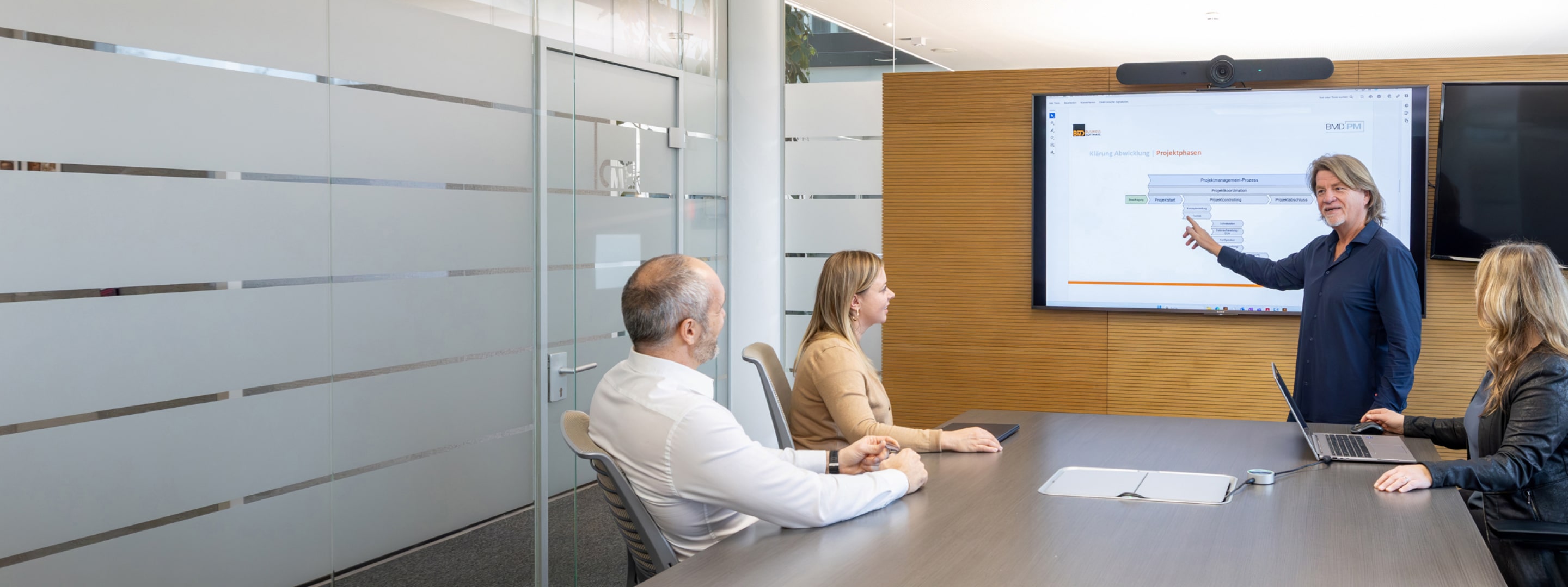 Das Team der BMD Projektbegleitung bei einer Besprechung in einem modernen Konferenzraum, mit Fokus auf einer Präsentation auf dem Bildschirm, die die Projektphasen erklärt.