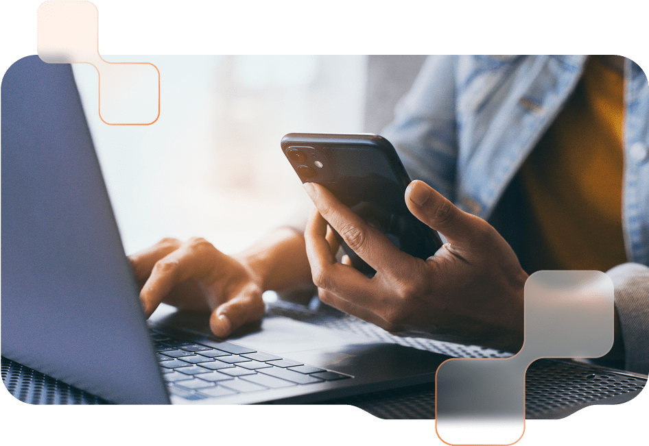 Eine Person arbeitet an einem Laptop und hält gleichzeitig ein Smartphone in der Hand.