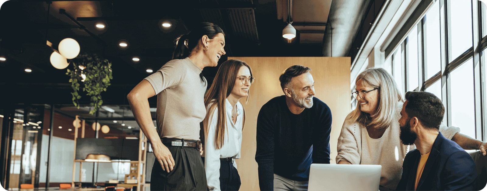 Header Software für Steuerberater Meeting in der Steuerberatungskanzlei: drei Damen und zwei Herren versammeln sich um ein Notebook im modernen Büro und lächeln.