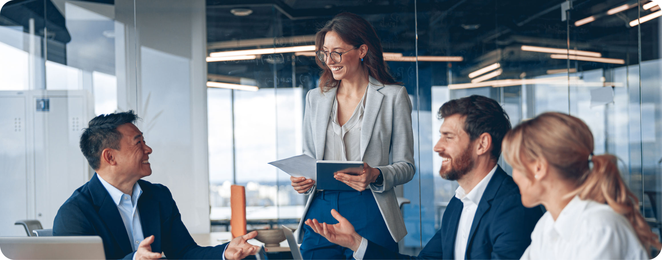 Unternehmenssoftware von BMD Ein Team aus vier Geschäftspersonen in moderner Büroatmosphäre. Eine Frau in einem hellen Blazer hält ein Tablet und lächelt, während sie mit ihren Kollegen spricht.