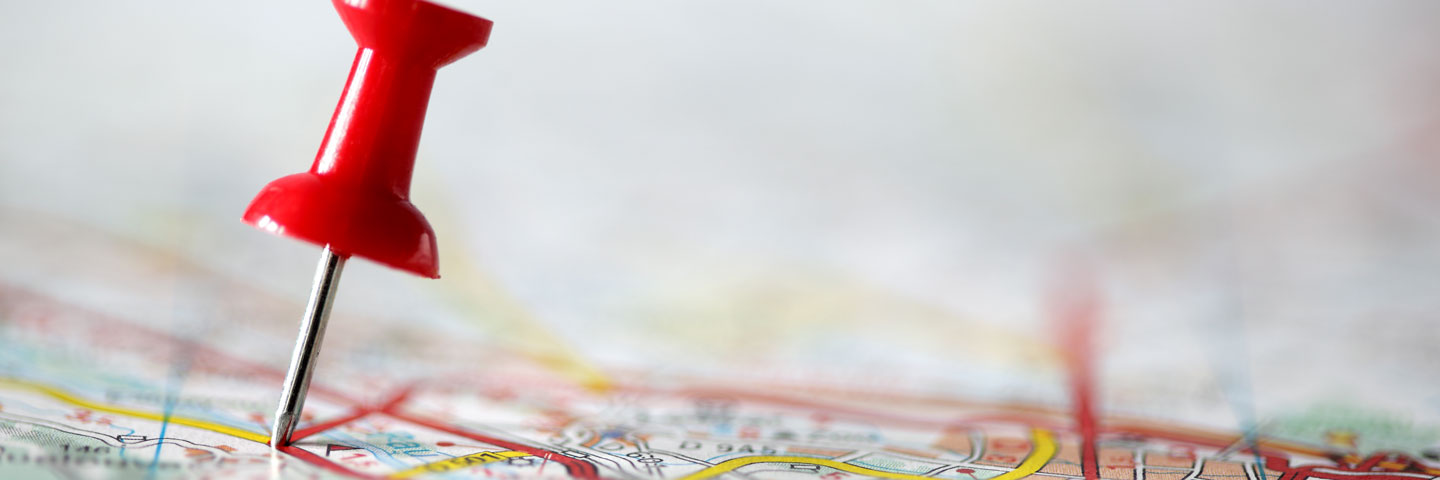 Nahaufnahme einer roten Stecknadel, die auf einer Landkarte platziert ist, um einen bestimmten Standort zu markieren.
