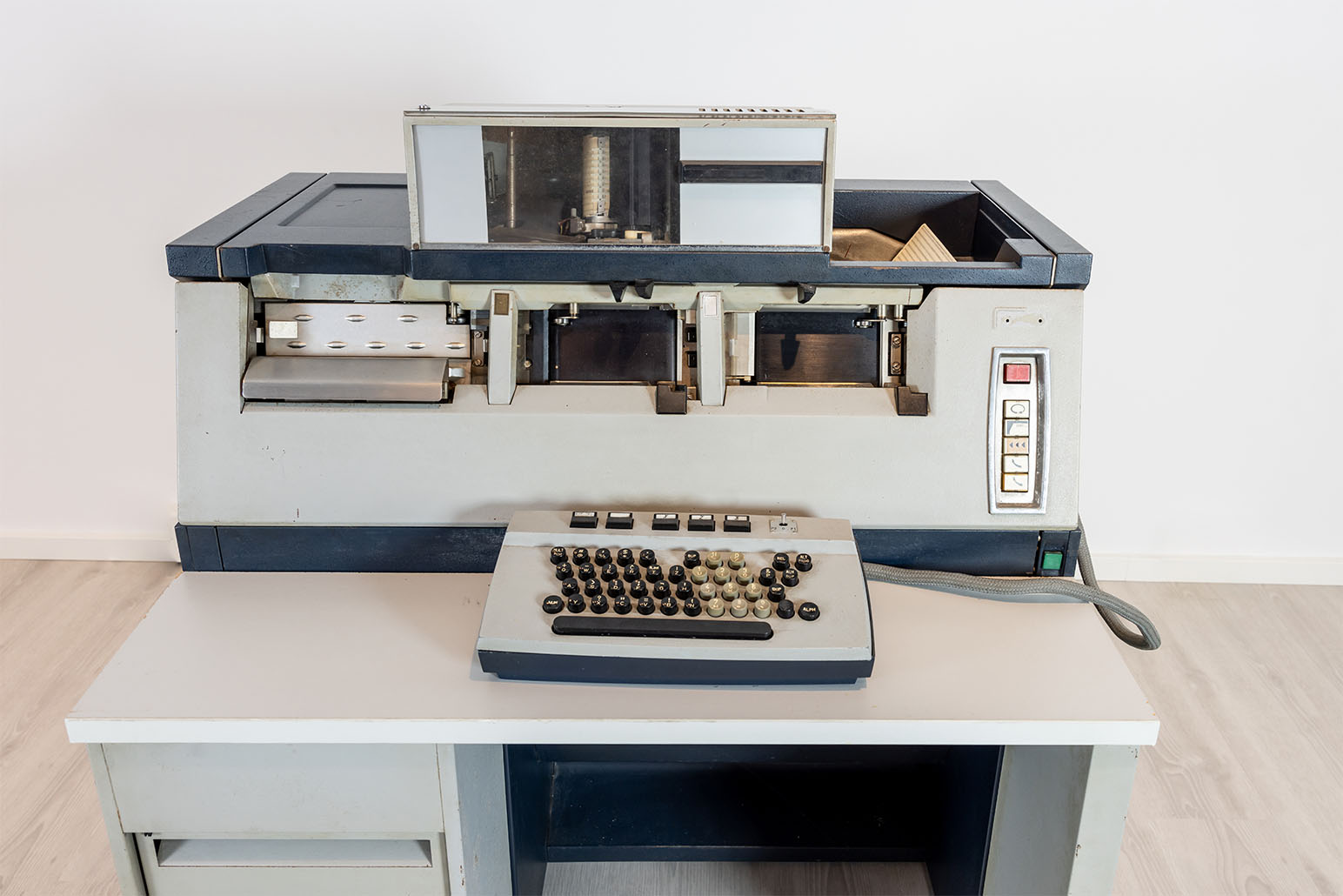 Weiß-grauer Lochkartenstanzer vor weißer Wand