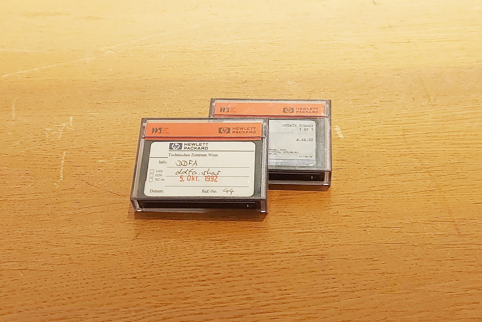 Kassetten in Plastikhülle mit weißem Kärtchen mit Beschriftung und Balken in oranger Farbe auf Holztisch