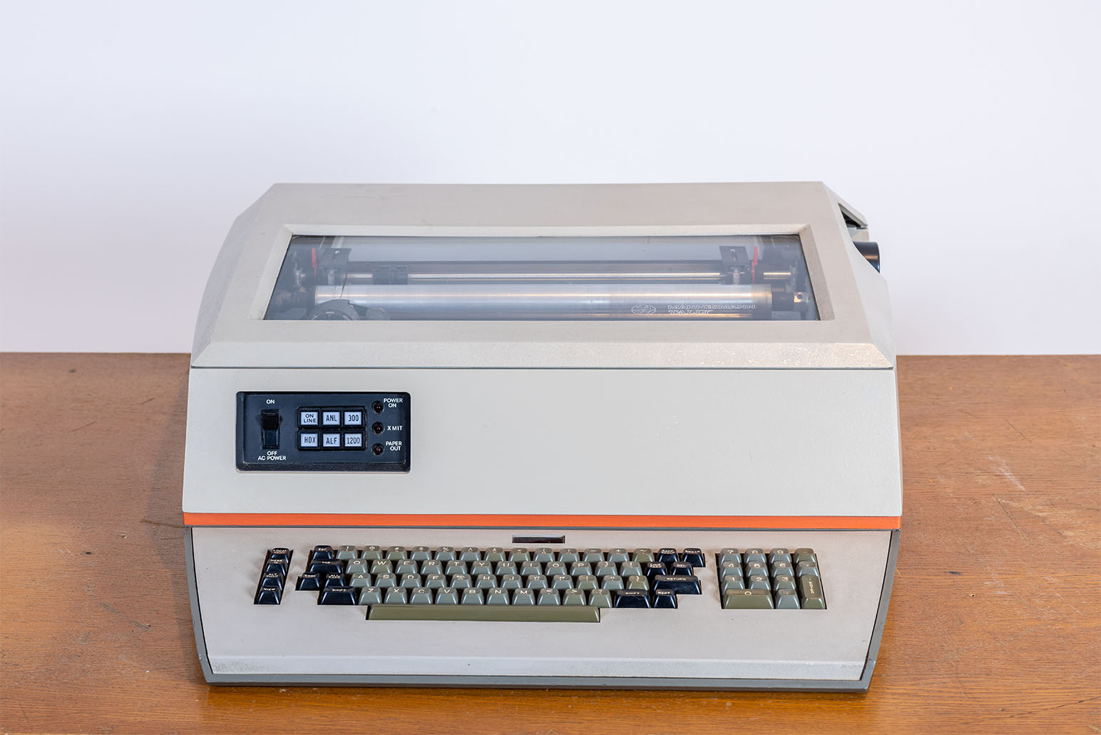 Grauer Nadeldrucker mit dunkleren Tasten und orangem Streifen auf Holztisch