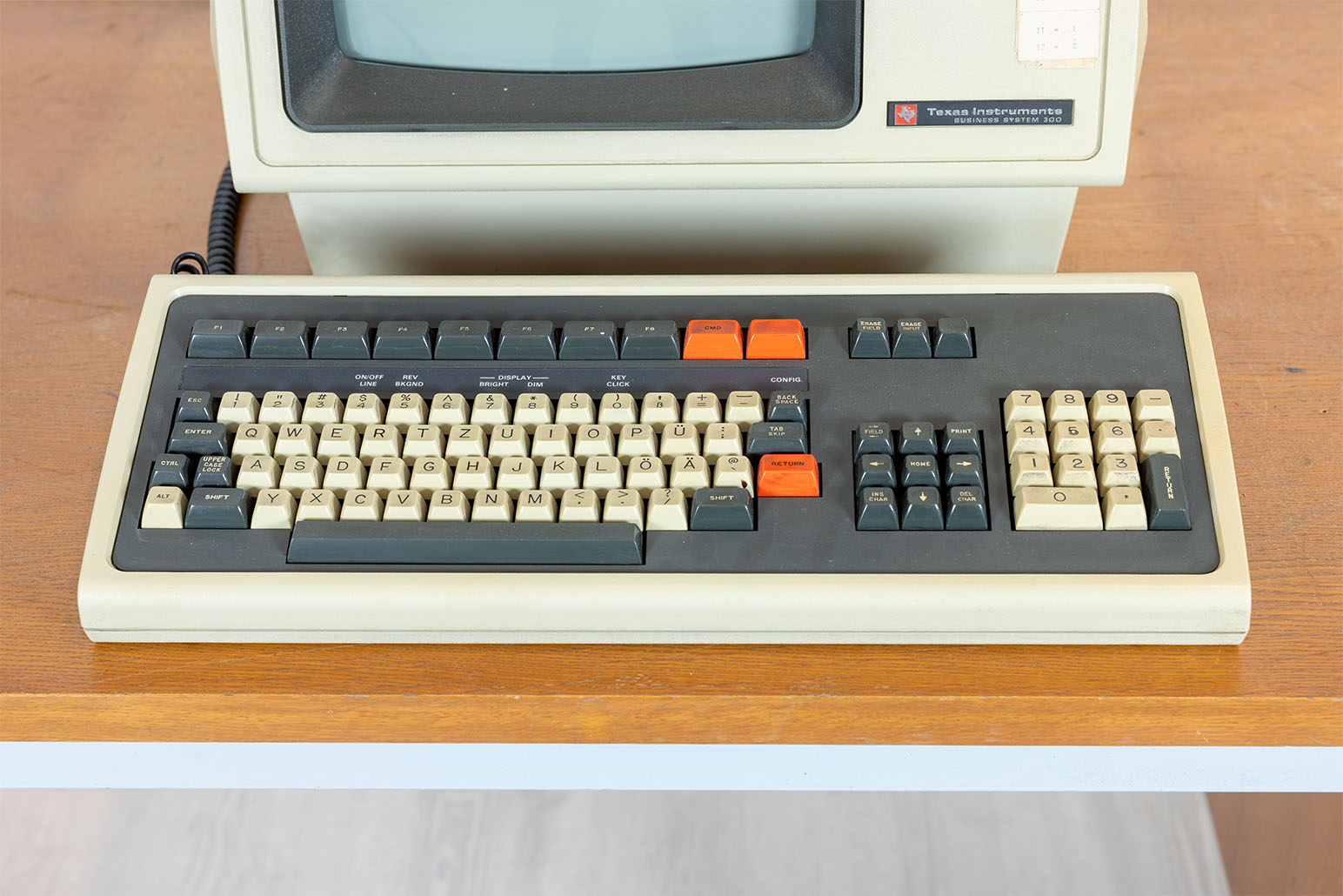 Beige-graue Tastatur (drei roten Tasten) auf Holztisch