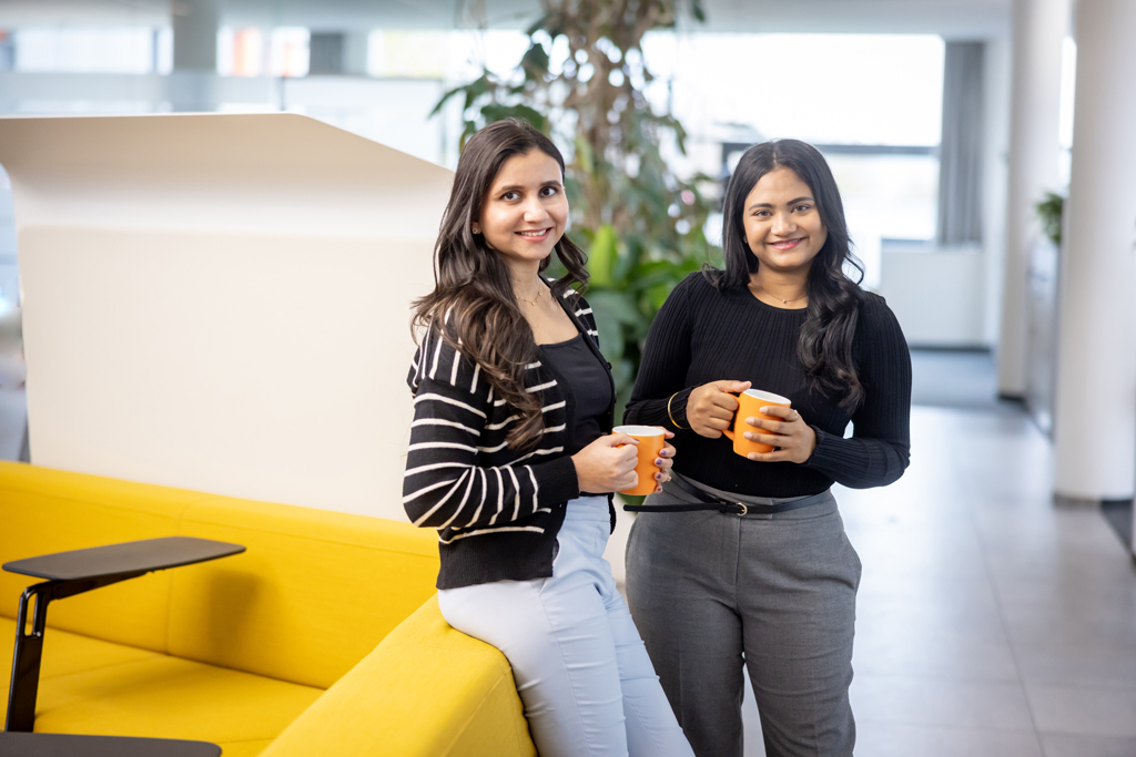 Zwei junge Frauen stehen mit Kaffeetasse in der Hand nebeneinander und lächeln in die Kamera. [© BMD, Gabor BOTA]