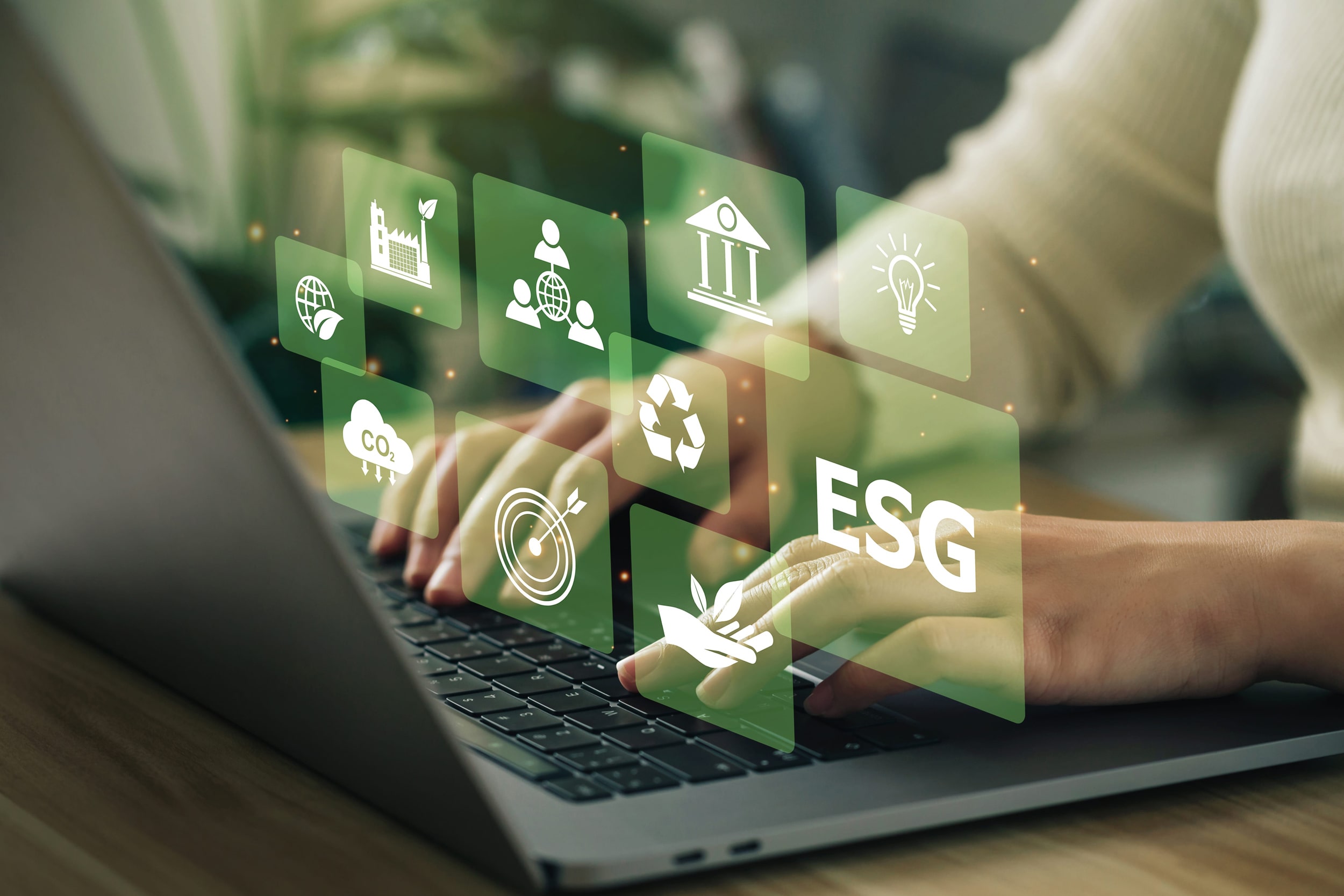 Hände einer Person, die am Notebook sitzt und tippt. Im Vordergrund sind verschiedene Icons zum Thema ESG abgebildet. [© Pcess609 - stock.adobe.com]