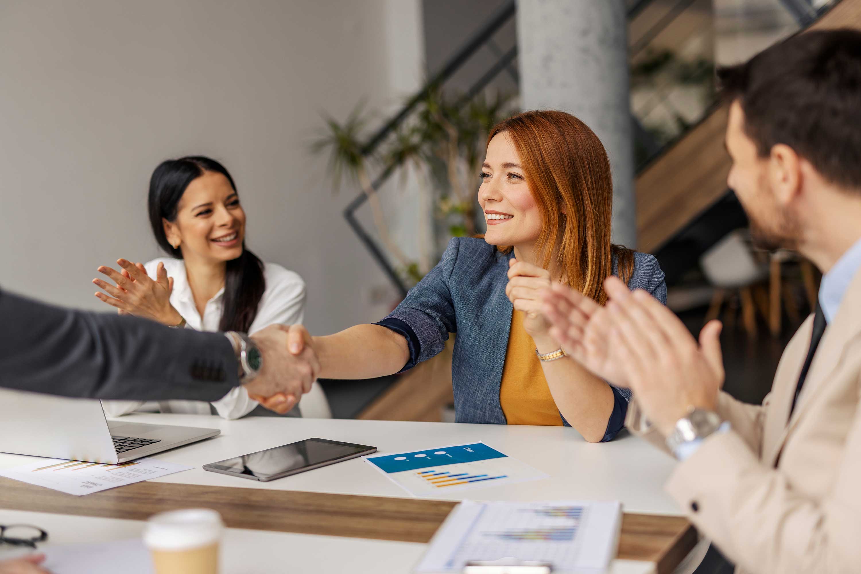 Eine Frau mit orangefarbenen Haaren lächelt und schüttelt einem Mann die Hand. Ein anderer Mann klatscht. 
