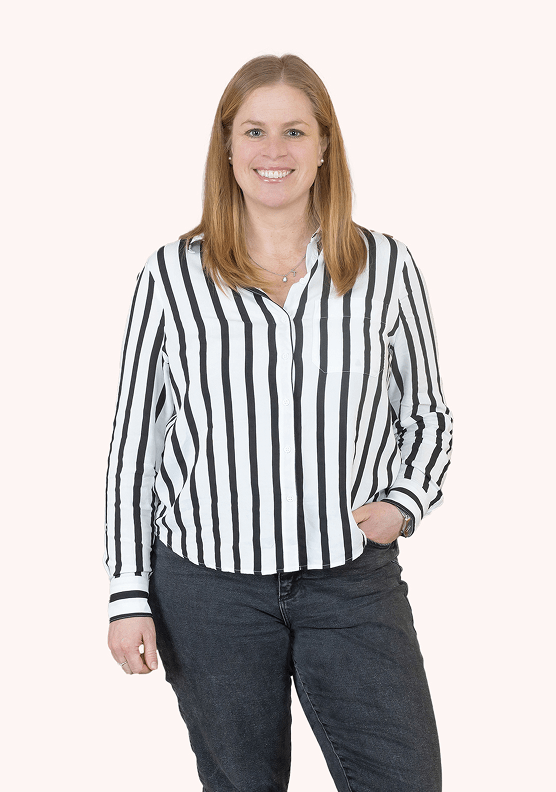 Eine Frau lächelt in die Kamera. Sie hat blondes Haar und trägt eine gestreifte Bluse und eine dunkle Jeans.