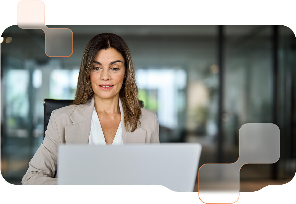 Frau im Business-Outfit vor einem Laptop. Im Hintergrund große Glasflächen eines modernen Büros.