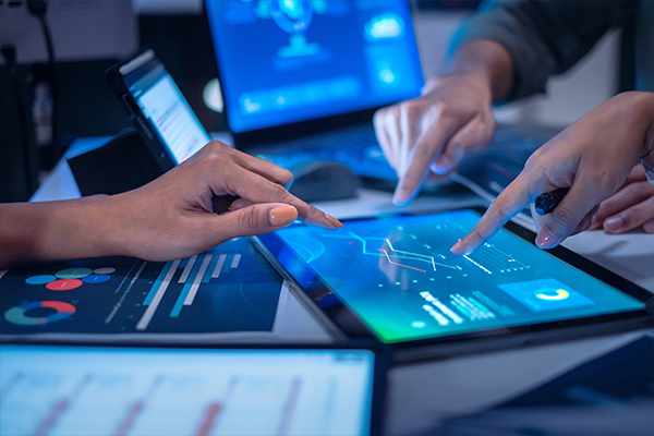 3 kéz látható, amely egy táblagépre mutat, amelyen különböző grafikák láthatók.