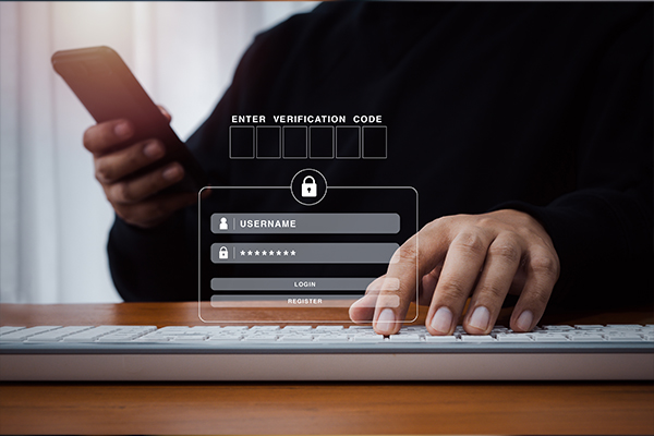 Egy férfit látsz, aki egyik kezével az okostelefonjába gépel valamit, a másik keze pedig egy laptopon van. Az előtérben megjelenik egy bejelentkezési mező.
