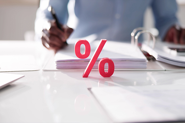 Egy férfit látsz, aki egy mappában lévő papírra ír valamit, előtérben egy nagy piros százalékos felirattal