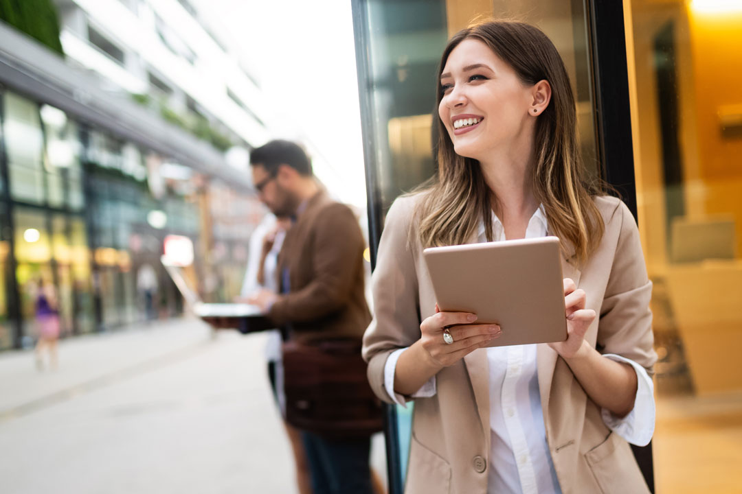 Vidíte usmievavú ženu s tabletom v ruke, ako stojí v meste